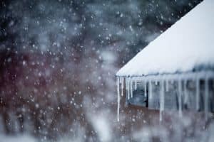 Snow-covered roof with long icicles forming along the edge during a winter snowfall.