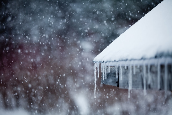 Snow-covered roof with long icicles forming along the edge during a winter snowfall.